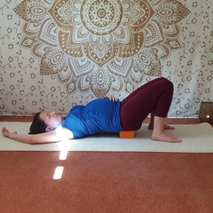 Marion ist schwanger und liegt in Rückenlage auf der Yogamatte. Die Beine sind vor dem Gesäß aufgestellt, das Becken ruht auf einem Yogaklotz. Die Position heißt gestützte Schulterbrücke oder indische Brücke und animiert das Baby, sich mit dem Kopf ins Becken zu drehen.